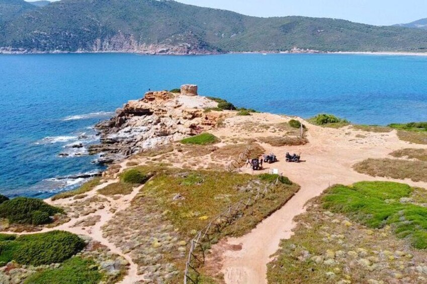 A coastal landscape with a rocky outcrop, a dirt path, and a small group of people. 3