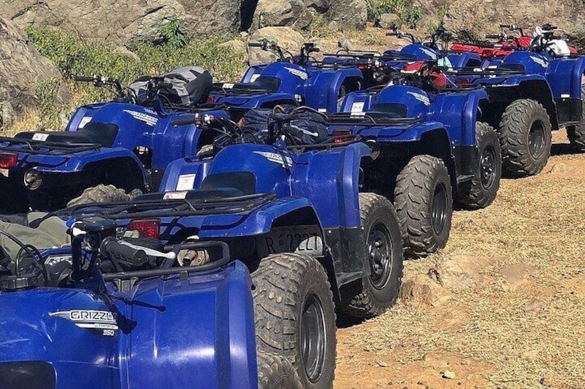 A row of blue ATVs parked on a dirt surface. 1