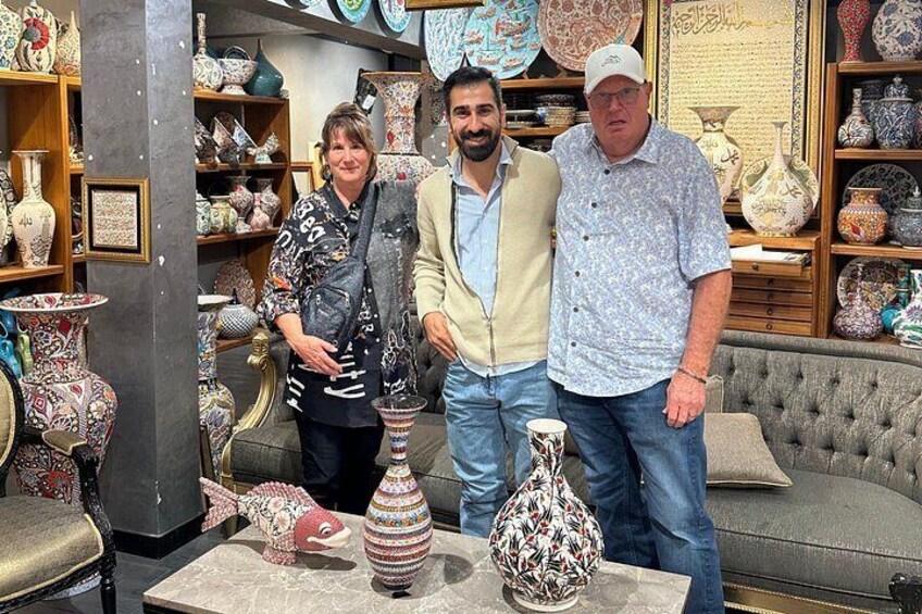 Three people in a pottery shop with various ceramic items on display. 4