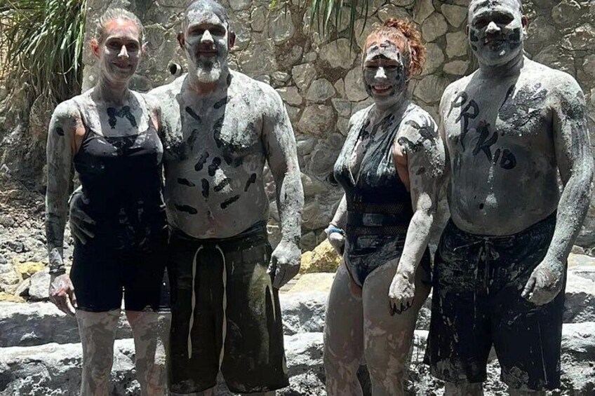 Four people covered in mud, standing in a rocky outdoor area. 1
