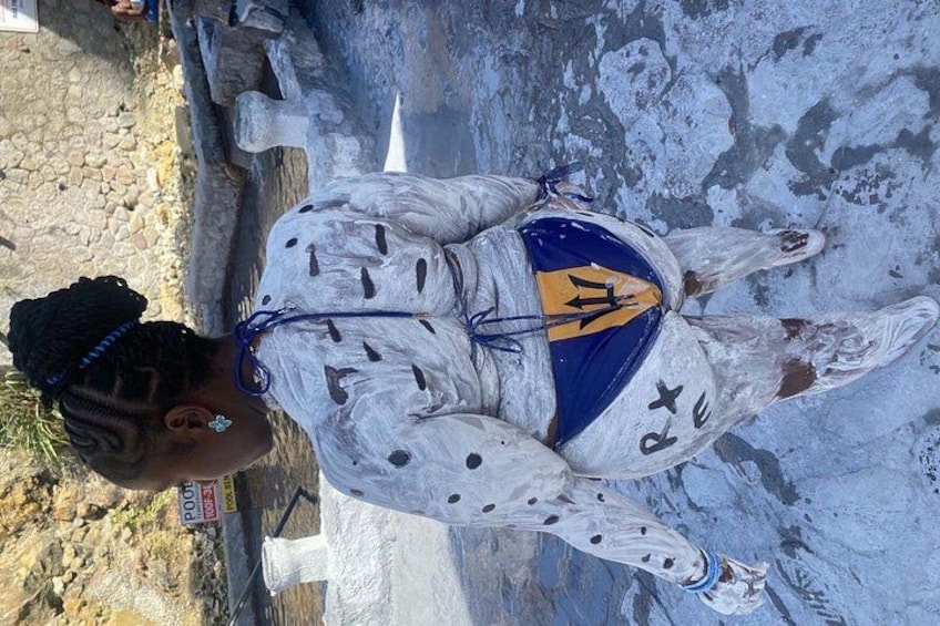 Una persona vestita di bianco, con dettagli blu e gialli, in piedi vicino a una struttura in pietra. 5