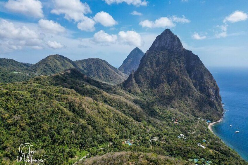 A mountainous landscape with a prominent peak, lush greenery, and a coastline with a few buildings. 4
