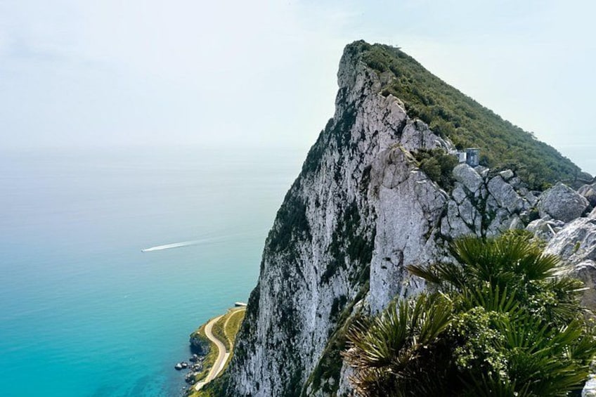 A coastal cliff with a road winding along the edge, a clear view of the ocean, and a small building on top of the cliff. 2
