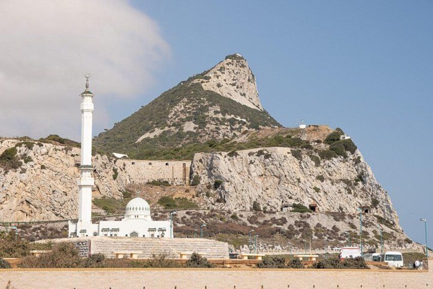 A mosque with a minaret and dome, set against a rocky hillside. 4