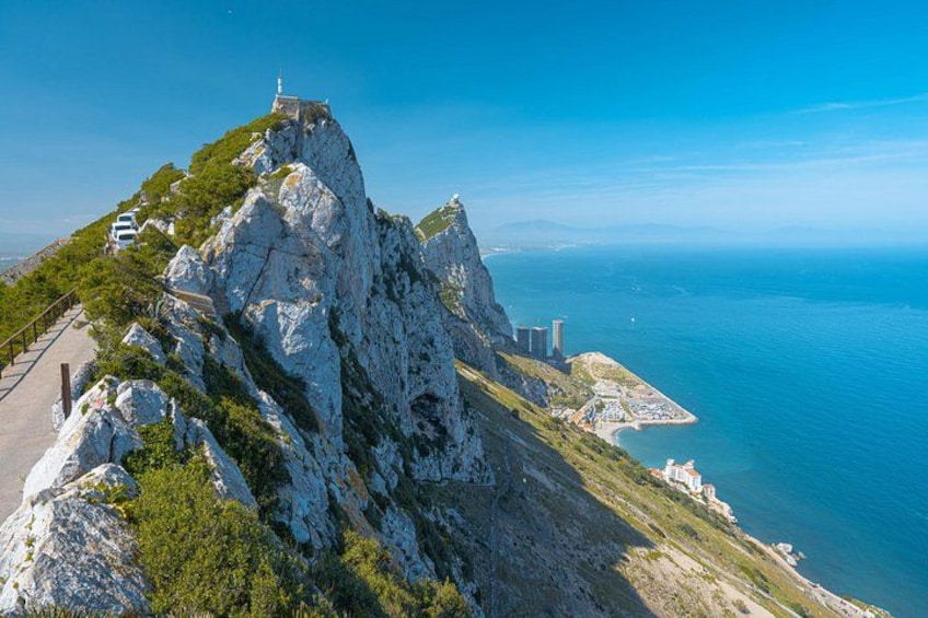 A coastal mountain with a lighthouse, a paved road, and a small settlement by the sea. 3