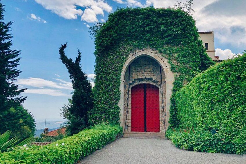 A red door with an arched stone frame, surrounded by lush green foliage. 3