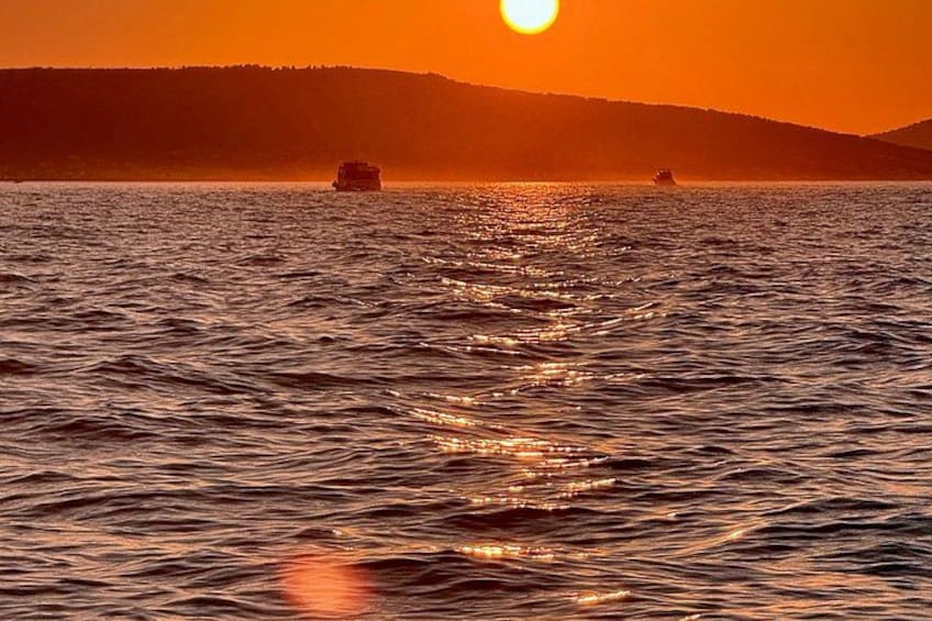 En solnedgång över ett vattenområde med båtar och en avlägsen kustlinje. 2