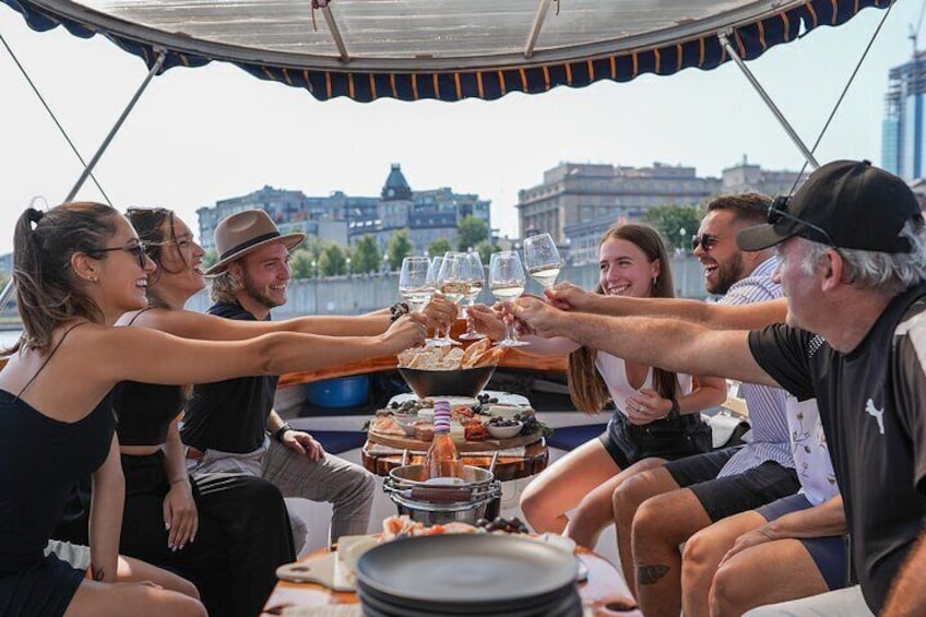 A group of people toasting with drinks on a boat with a cityscape in the background. 2