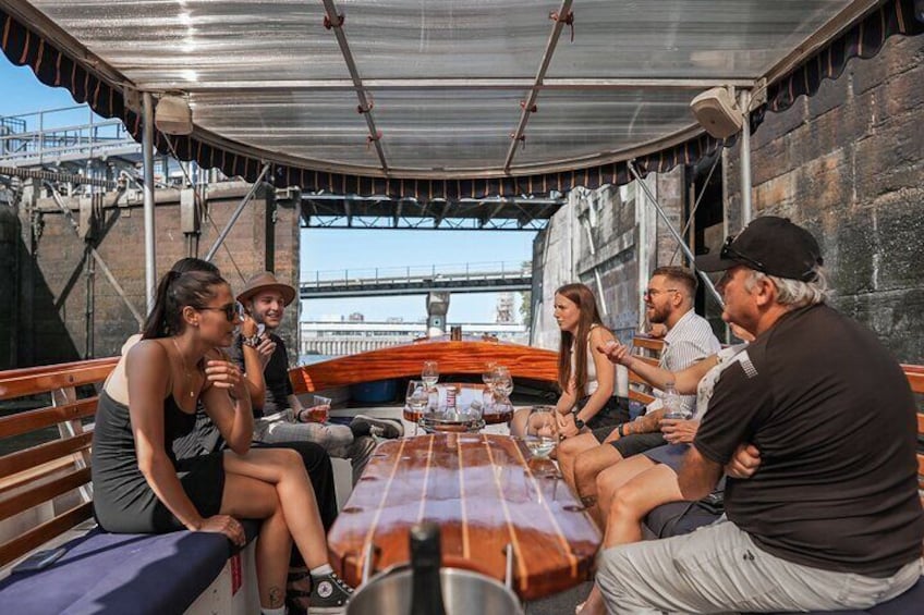 A group of people sitting around a wooden table under a metal roof, overlooking a body of water. 1