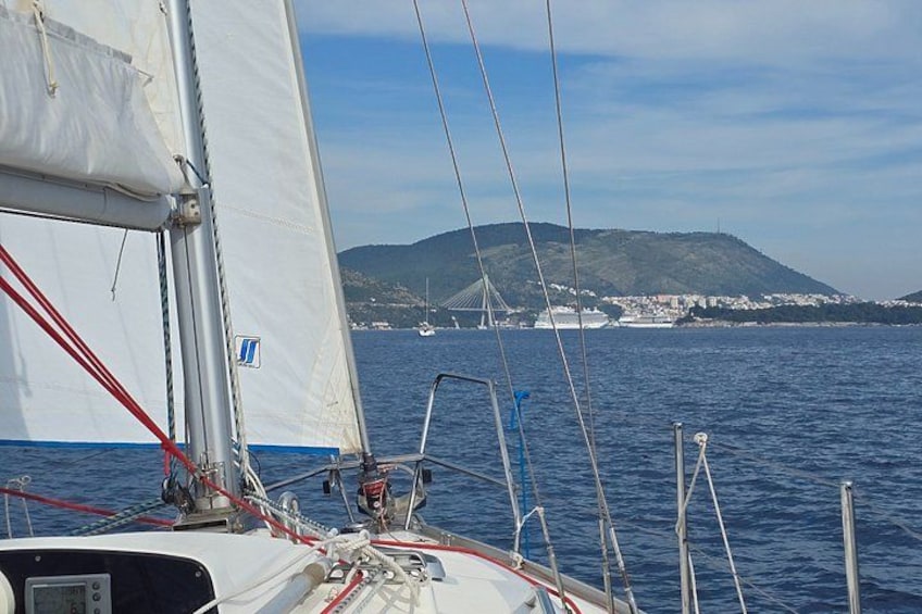 Een zeilboot met een witte zeil, rode lijnen en een uitzicht op een brug en heuvels in de verte. 5