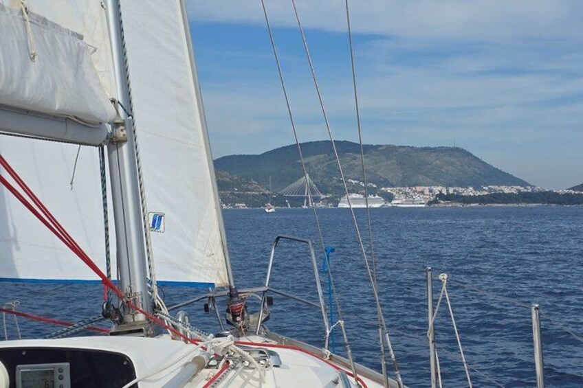 Un velero con vela blanca, aparejo rojo y una vista de un puente y colinas al fondo. 5