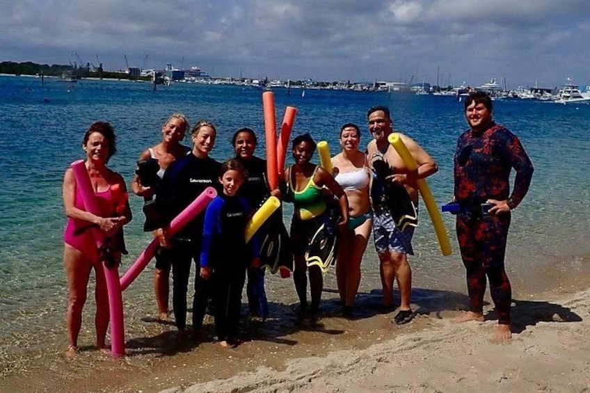 A group of people at a beach with surfboards and a clear blue sea. 2