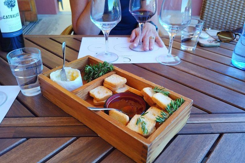 A wooden tray with bread, a bottle of wine, and glasses on a table. 5