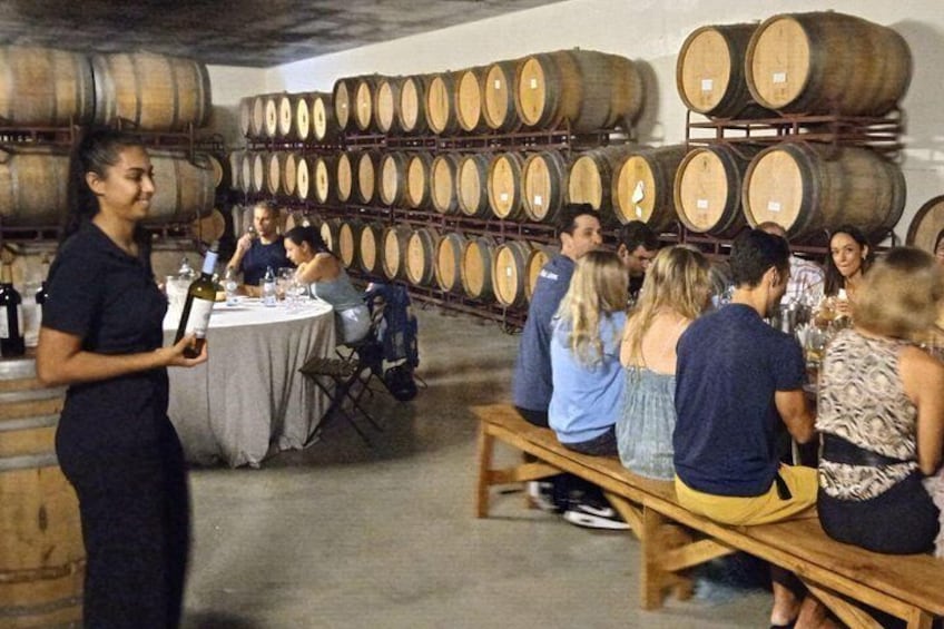 A group of people seated at a table in a cellar with wine barrels in the background. 2