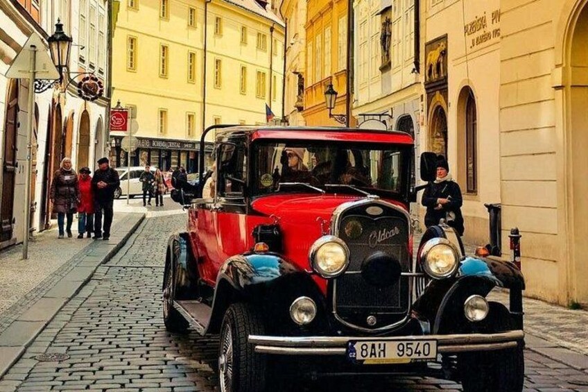 A vintage red car parked on a cobblestone street in a European city. 4