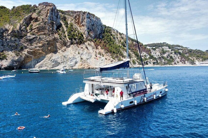 Una barca bianca con una vela sull'acqua, circondata da scogliere rocciose e altre imbarcazioni. 1