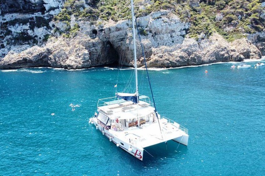 Un catamarano bianco naviga in acque blu cristalline vicino a scogliere rocciose. 4