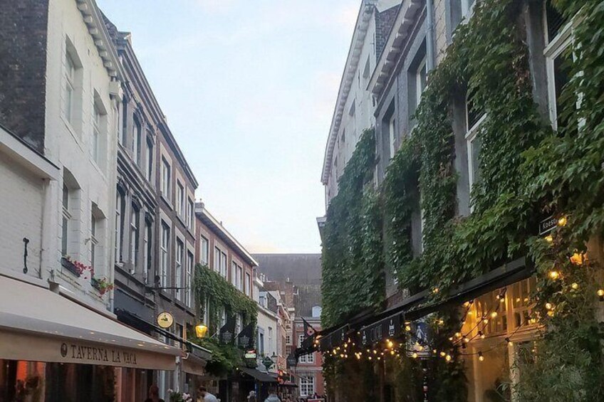 Una calle estrecha flanqueada por edificios, algunos con hiedra y luces colgantes. 1