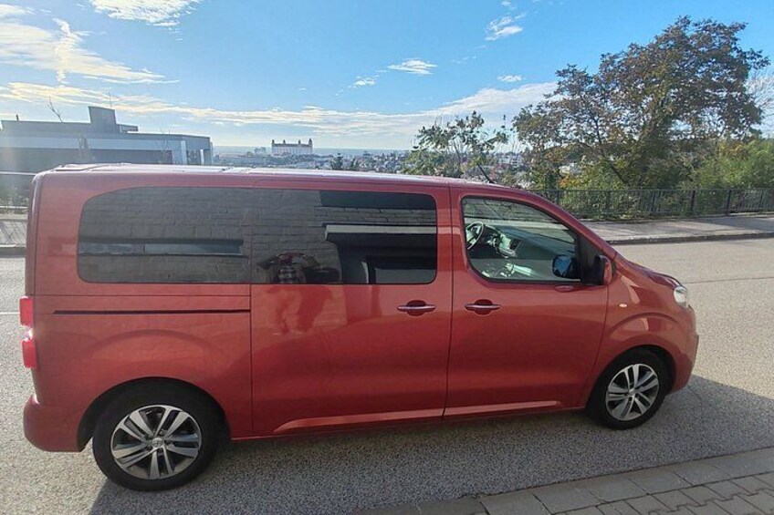 A red van parked on a paved area with a clear sky and distant buildings in the background. 2