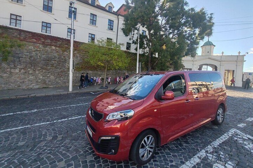 A red car parked on a cobblestone street with buildings and a church in the background. 4
