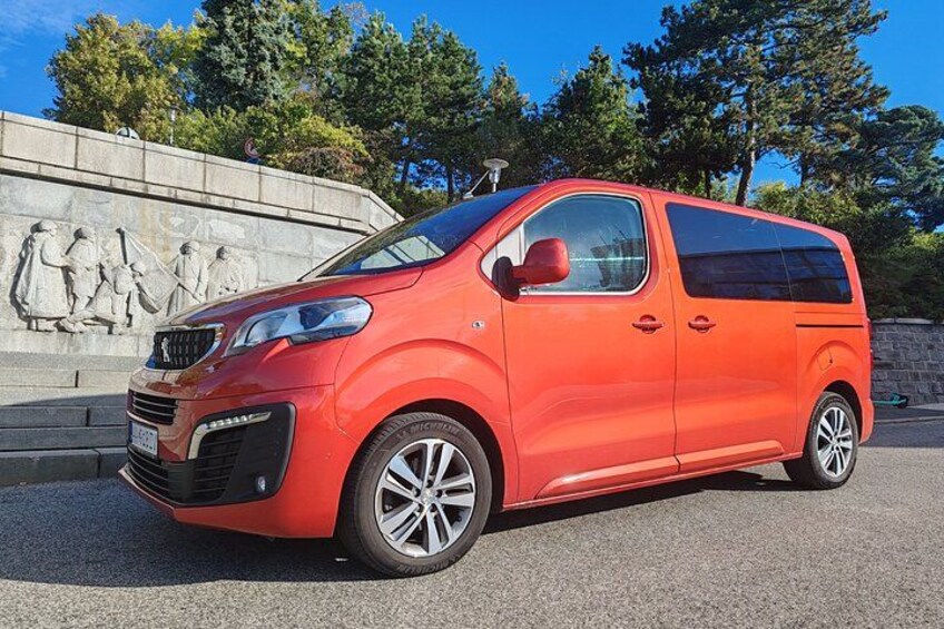 A red minivan parked in front of a stone monument with a clear blue sky in the background. 5