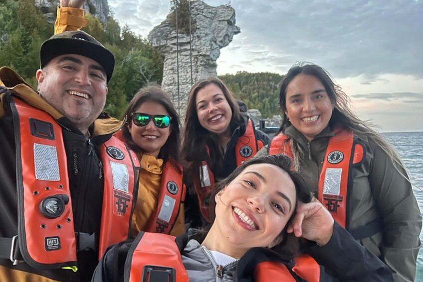 Un grupo de personas con chalecos salvavidas se toman un selfie cerca de un acantilado rocoso junto al mar. 1