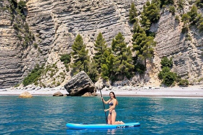 Une personne fait de la planche à pagaie sur une étendue d’eau calme, avec une côte rocheuse et des arbres en arrière-plan. 4