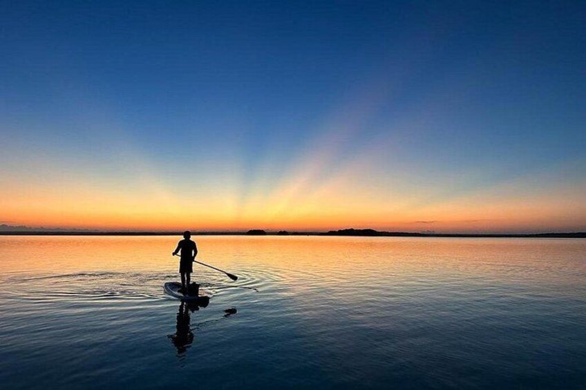 Une personne pratiquant le stand-up paddle sur une eau calme au coucher du soleil. 1