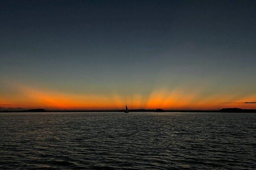 A sunset over a calm sea with a sailboat in the distance. 4