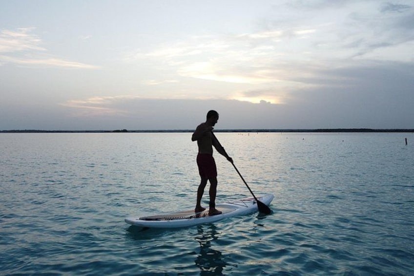 A person paddleboarding on calm water during sunset. 5