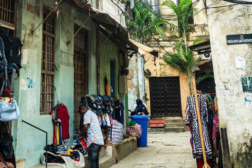 A street with a man standing near a pile of bags, a blue trash bin, and clothes hanging on a line. 2