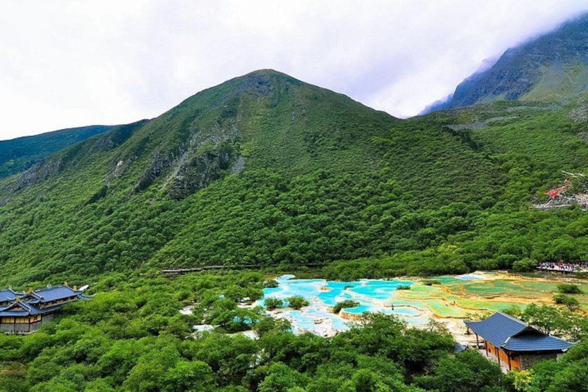 A mountainous landscape with lush greenery, a turquoise lake, and traditional buildings. 4