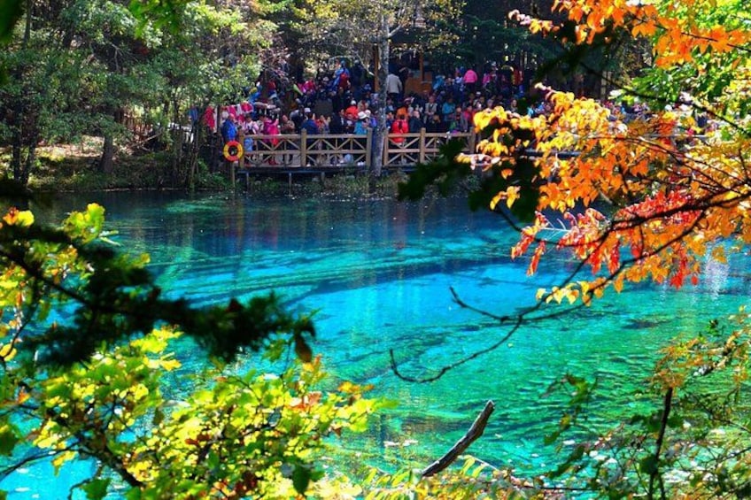 A clear blue lake with a wooden bridge and people on it. 1