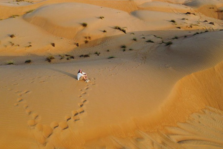 Une personne assise sur une dune de sable, avec des empreintes de pas qui mènent jusqu'à elle. 2