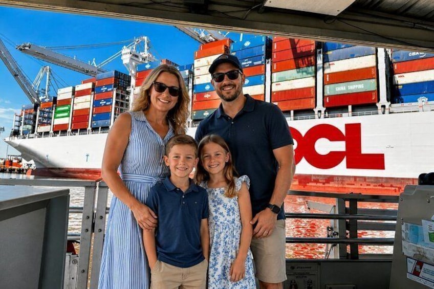 Una famiglia che si posa davanti a una nave cargo con container e il logo 'DHL'. 5