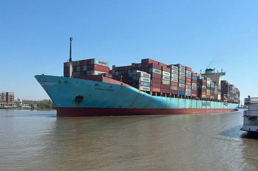 A large cargo ship with multiple containers stacked on its deck, sailing in a river. 2