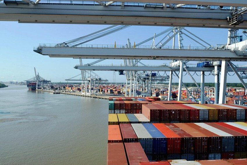 A port with multiple shipping containers stacked in rows, large cranes, and a body of water. 4