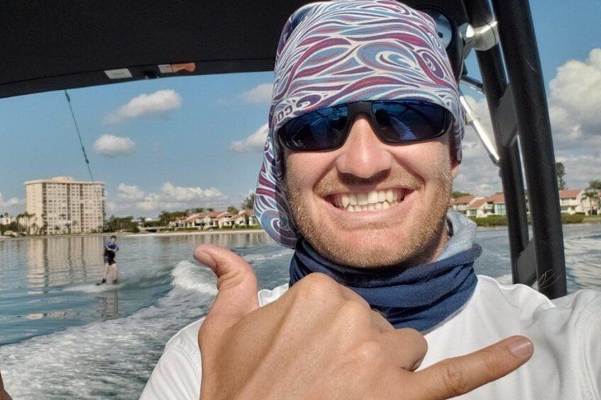 Une personne se trouve sur un bateau, et on aperçoit un pratiquant de wakeboard à l'arrière-plan. 4