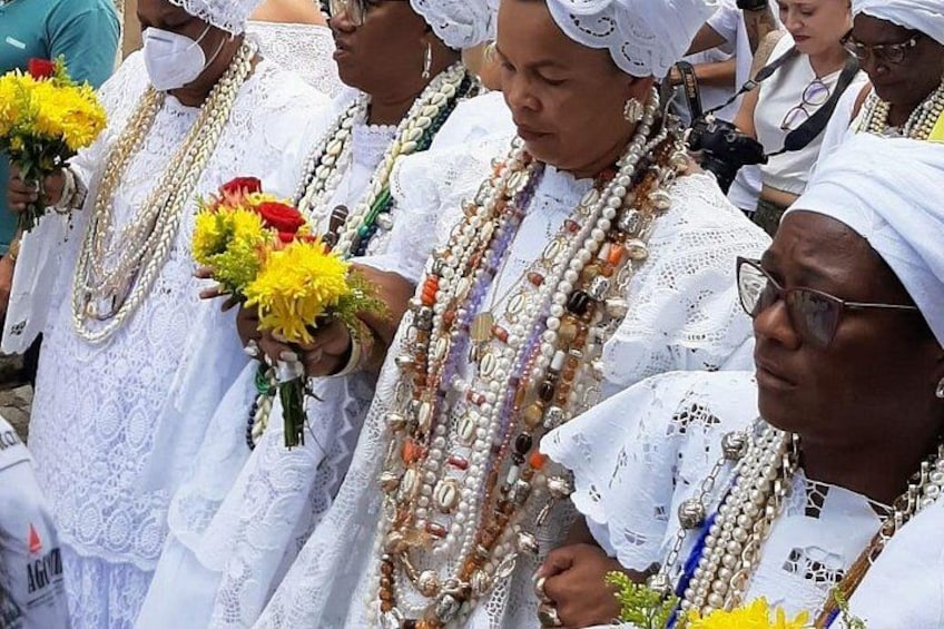 Un grupo de personas vestidas de blanco con collares de cuentas elaborados y sosteniendo flores amarillas. 2