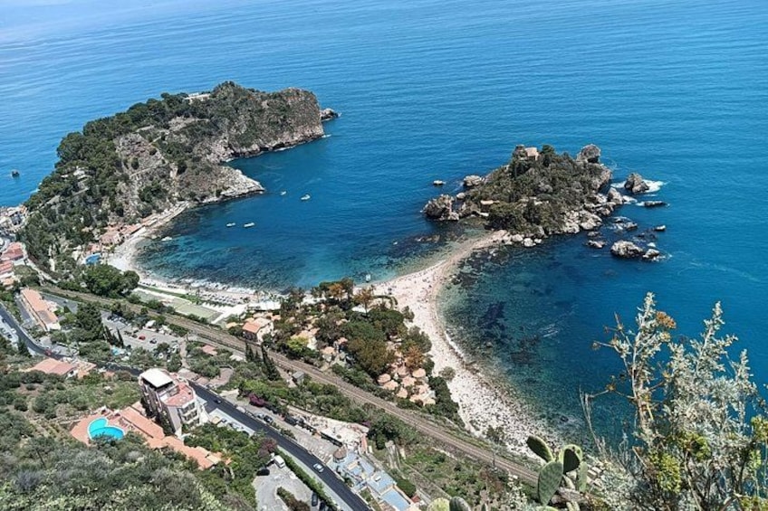 Un paysage côtier caractérisé par des îles rocheuses, des eaux d’un bleu limpide et une route menant à une plage. 1