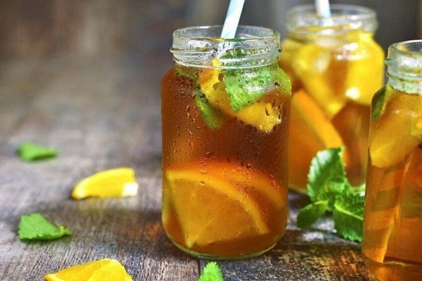 A glass jar with a straw, containing a beverage with ice cubes and lemon slices, surrounded by mint leaves on a wooden surface. 4