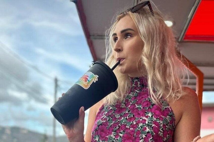 A person holding a black tumbler with a colorful logo, wearing a floral dress, and standing outdoors. 3