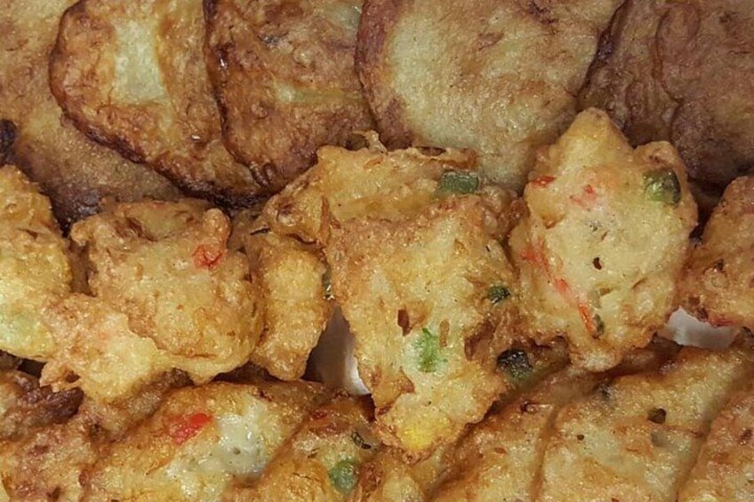 A close-up of fried food items, likely fritters or pancakes, with visible green and red specks, possibly herbs or spices. 5