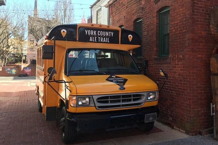 En gul bus fra York County Ale Trail parkeret på en brostenbelagt fortov. 1