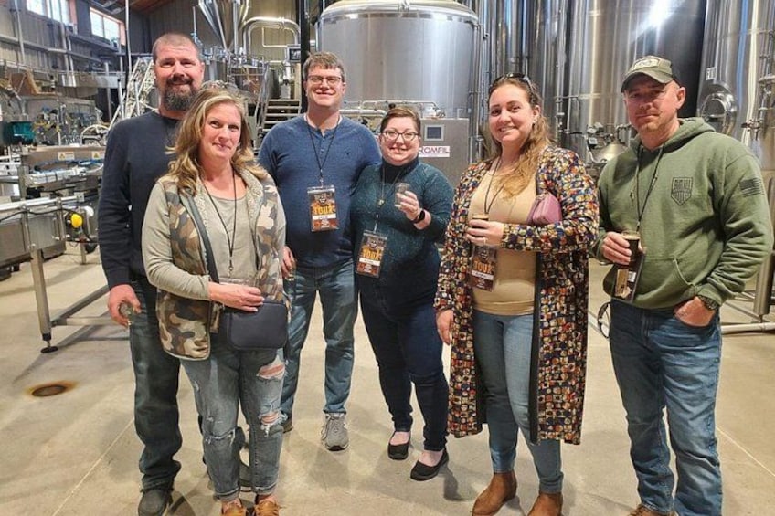 A group of people in a brewery holding beer bottles. 3