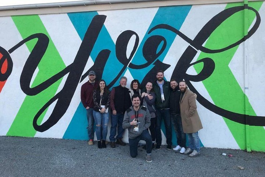 A group of people posing in front of a colorful wall with large, stylized text. 5