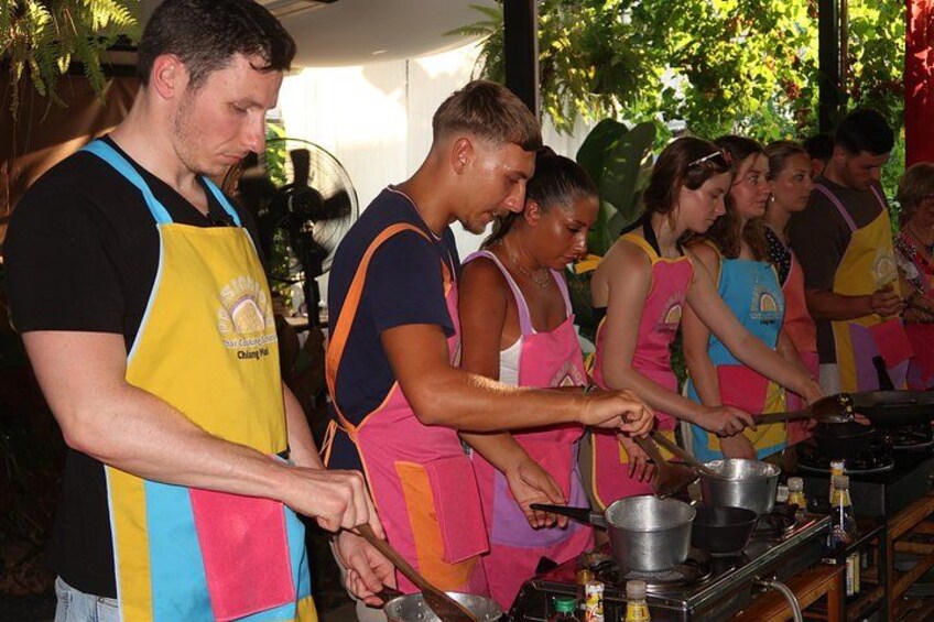 People cooking outdoors, wearing aprons, with cooking equipment and ingredients visible. 4