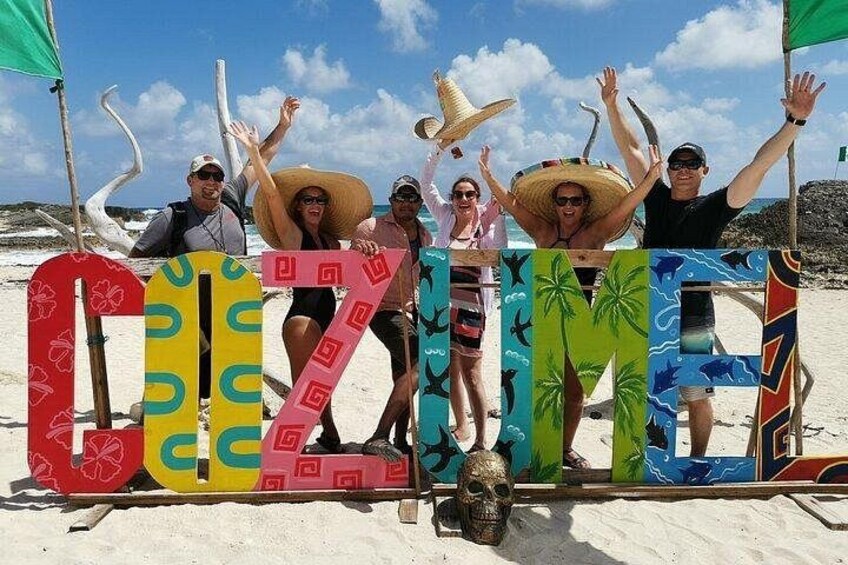 Persone su una spiaggia con lettere colorate che formano la parola 'CINEMA' e un cappello tiki. 2