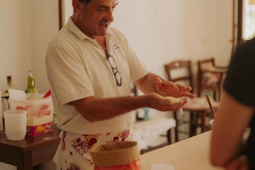 A person in a white shirt and apron preparing food, with a table and chairs in the background. 3