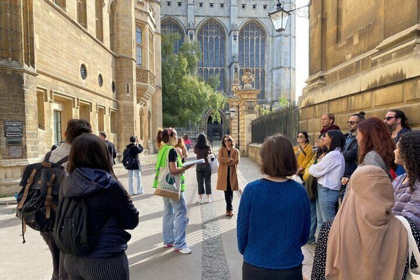 A group of people standing on a street in front of a historic building with large windows and a gate. 1